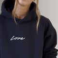 Woman wearing black hoodie with white 'Love' script, fitness apparel fashion