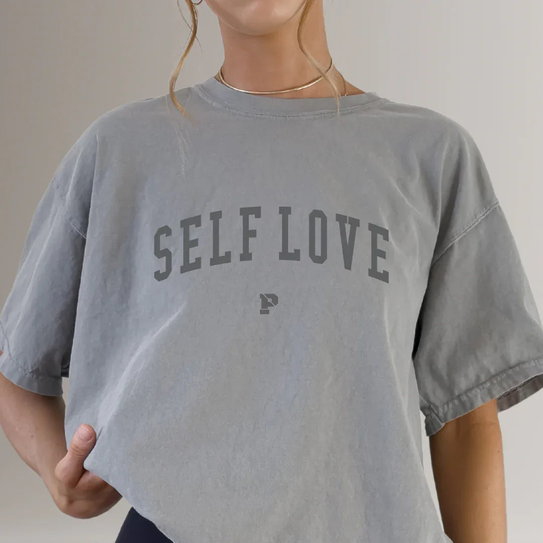 Woman wearing oversized grey t-shirt with 'SELF LOVE' text, fitness apparel