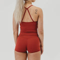 Woman wearing red fitness tank top and matching workout shorts, back view, studio lighting